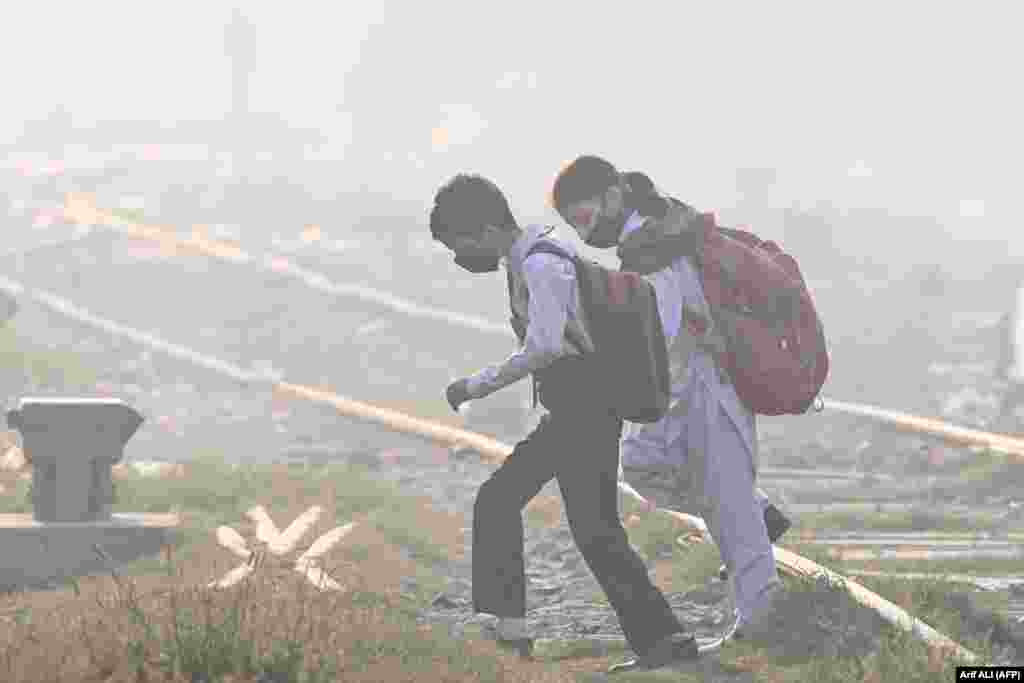 Pakistani schoolchildren wearing masks walk across a railway track amid thick smog in Lahore.&nbsp;