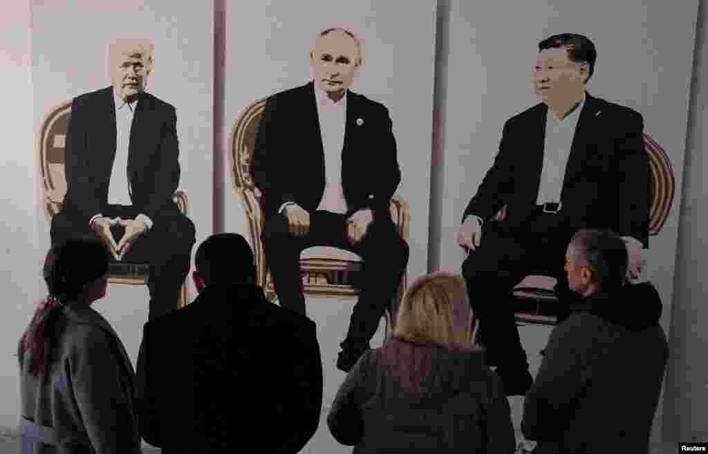 Visitors stand in front of an artwork depicting U.S. President Donald Trump (left), Russian President Vladimir Putin (center), and Chinese President Xi Jinping at an exhibition titled Yalta 2.0 in the occupied Ukrainian peninsula of Crimea. 