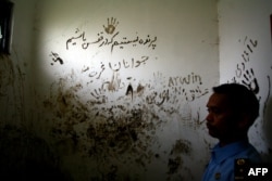 An Indonesian official stands next to graffiti that reads, "We are not birds to be locked inside a cage" in the room where a tunnel was dug by asylum seekers at a detention center in Pasuruan, East Java, in 2012.