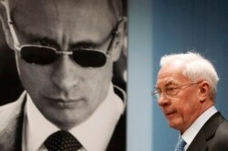 Mikola Azarov, în exil la Moscova, trece prin fața unui portret al lui Putin.