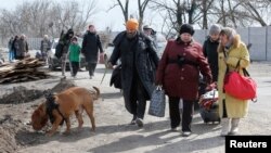 Мужчина с собакой вместе с другими жителями Мариуполя направляется к месту эвакуации из осажденного российскими войсками города, 20 марта 2022 года