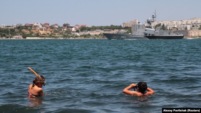 Отдыхающие на фоне российского военного корабля. Севастополь, 2019 год