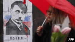 Not the first time: A woman walks in front of a poster in Kyiv on March 3 depicting Russian President Vladimir Putin as Adolf Hitler and signed "Hands off Ukraine."