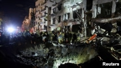 Ekipet izraelite të emergjencës inspektojnë një krater në vendin ku ka rënë një projektil, pas lëshimit të raketave nga Irani drejt Izraelit, në Tel Aviv.