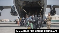 Afgán családoknak segít felszállni egy amerikai tengerészgyalog az amerikai légierő Boeing C-17 Globemaster gépére az evakuálás során a Hamid Karzai nemzetközi repülőtéren, Kabulban 2021. augusztus 23-án