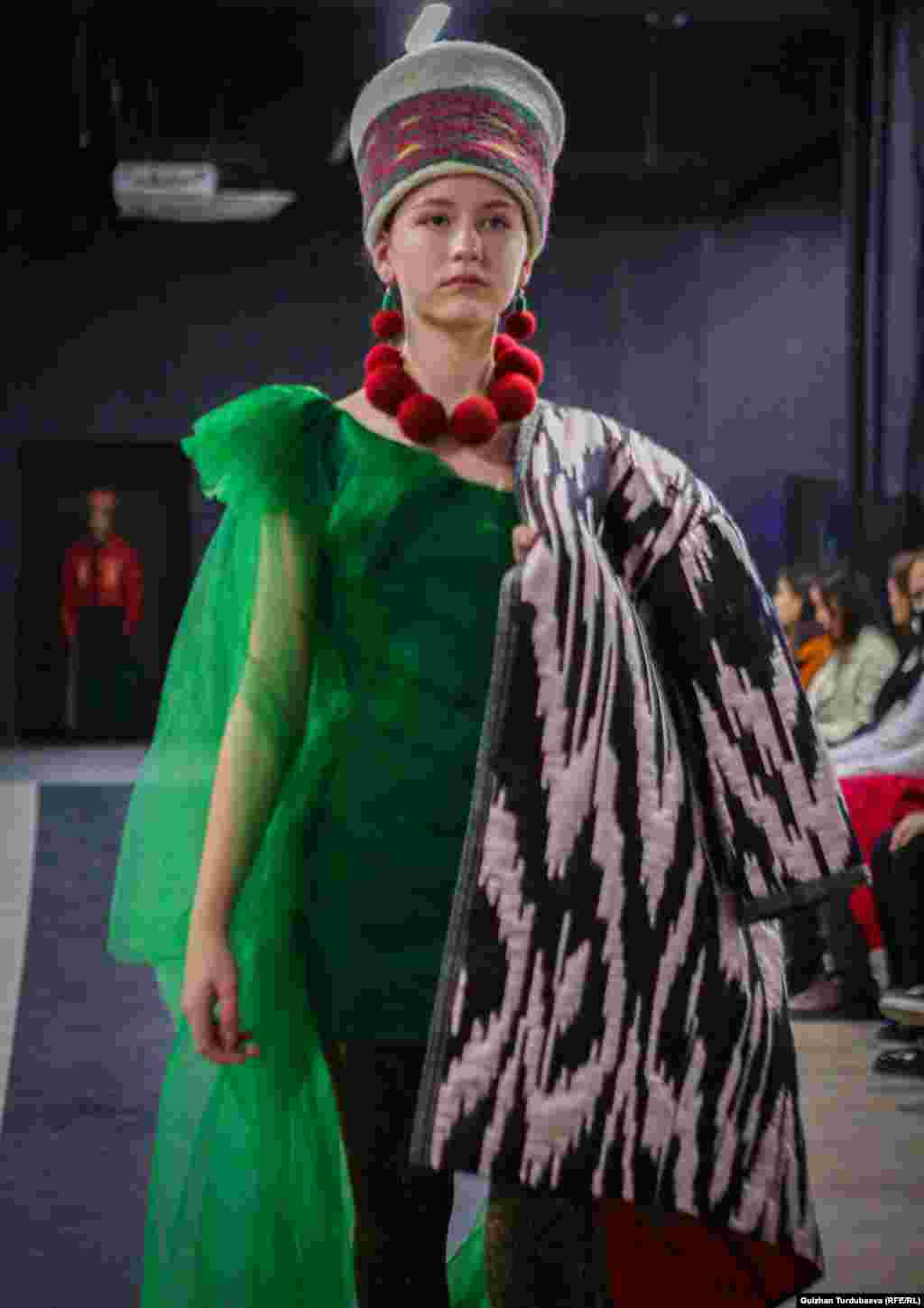 Чолпон Антонисес создала образ из атласного чапана и зеленого платья. Образ дополнен головным убором, напоминающим кыргызский элечек, на шее модели - крупные войлочные бусы насыщенно-красного цвета.