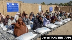 Afghans sit beside sacks of food grains distributed as aid by the World Food Programme in Kandahar on October 19.