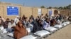 Afghans sit beside sacks of food grains distributed as aid by the World Food Program in Kandahar on October 19.