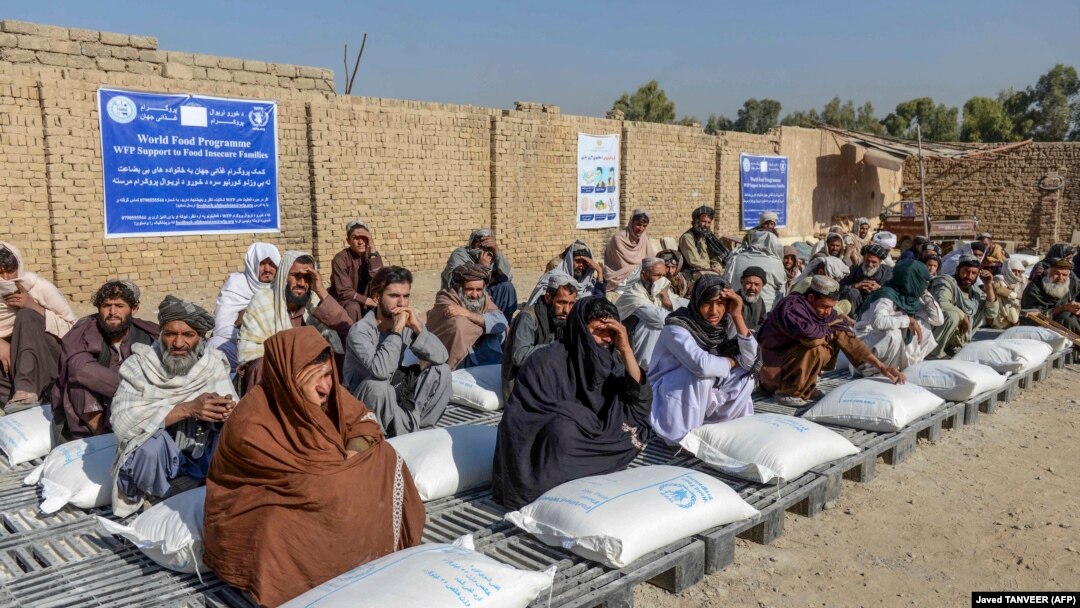 Afghans sit beside sacks of food grains distributed as aid by the World Food Program in Kandahar on October 19.