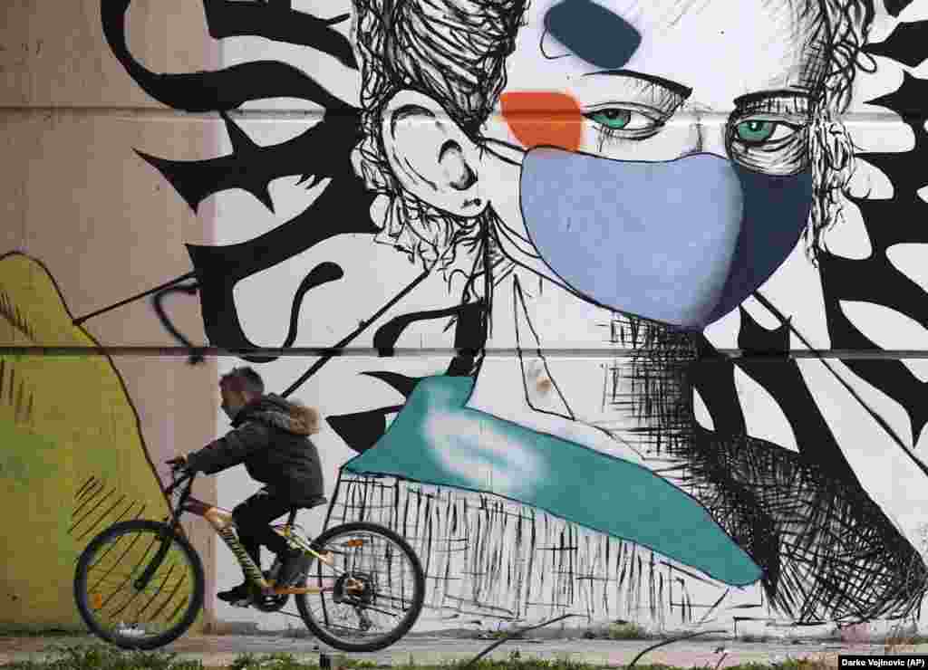 Мальчик проезжает на велосипеде мимо граффити в городе Митровица на юге Косова