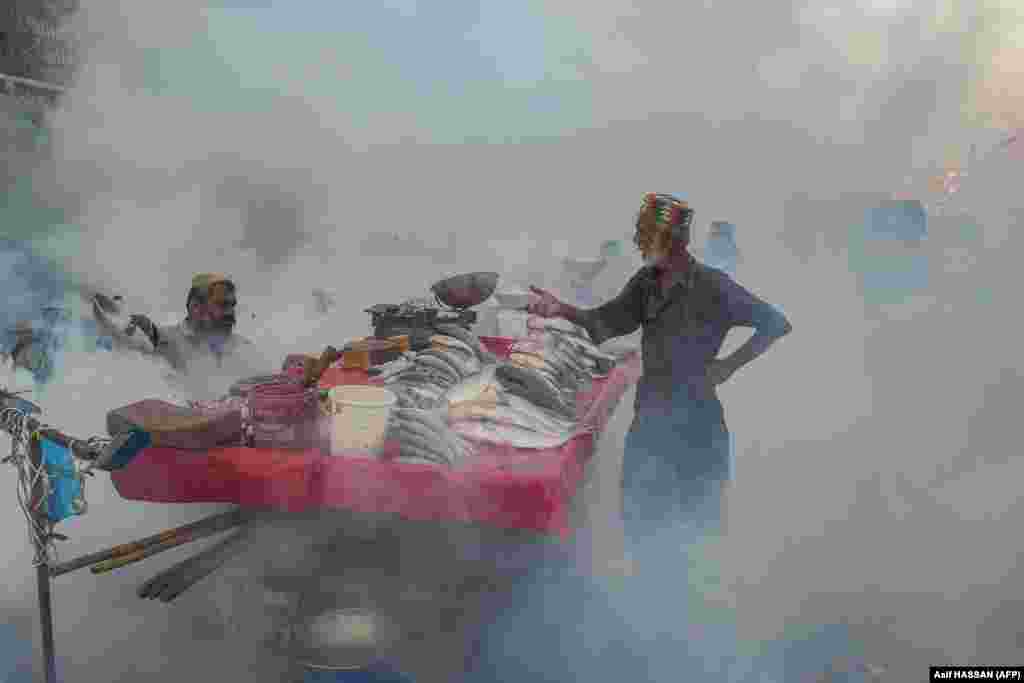Vânzători de pește își afumă marfa ca măsură preventivă împotriva țânțarilor purtători de boli, într-o piață din Karachi, Pakistan.