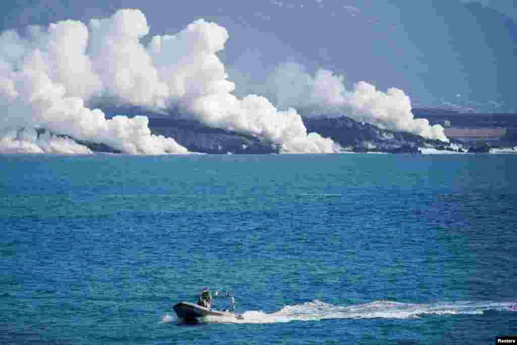 Човен іспанської цивільної гвардії пропливає морем, а з моря піднімається пара і дим від стікання лави у воду. Вигляд із порту Тазакорте, Канарський острів Ла-Пальма, Іспанія, 6 жовтня 2021 року