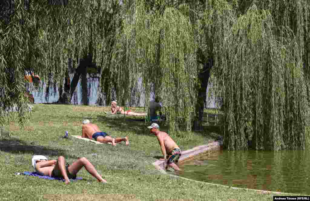 Oameni fac plajă lângă lacul din Parcul Alexandru Ioan Cuza din București.