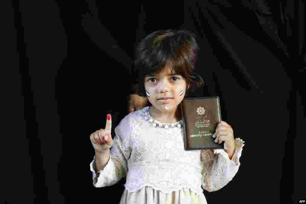 An Iranian girl shows her ink-stained finger and her mother's ID after the latter voted in a presidential election at in southern Tehran on May 19. (AFP/Atta Kenare)