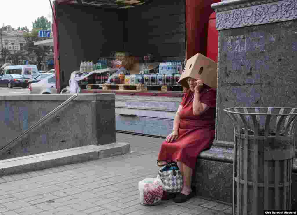 An elderly Ukrainian woman covers her head from the sun as she begs for money in central Kyiv on July 26. (Reuters/Gleb Garanich)