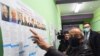 Кандидат Борис Вишневский показывает на избирательный стенд с двумя своими двойниками