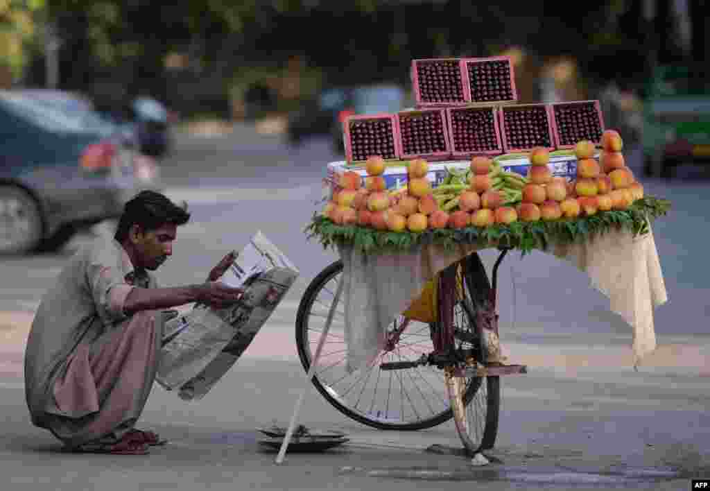 A Pakistani fruit vendor reads a newspaper as he waits for customers on a street in Islamabad. (AFP/Aamir Qureshi)
