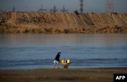 An Afghan man transports containers of water in a wheelbarrow alongside the Amu River on the border of Afghanistan and Uzbekistan.