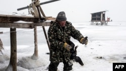 Рибар се обидува да ослободи птица заглавена во замрзнатото Дојранско Езеро на 11 јануари 2017