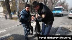 Полиция өкілдері ұстаған адамды "Астана" алаңы маңында тұрған көлікке салуға әкеле жатыр. Алматы, 22 ақпан 2020 жыл.