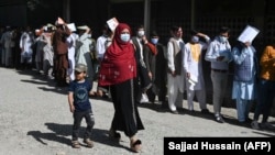Паспорт алуға өтініш тапсыруға кезекте тұрған адамдардың қасынан өтіп бара жатқан бала жетектеген әйел. Кабул, Ауғанстан, 25 шілде 2021 жыл.