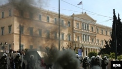 Грек парламентинин сырт жагында турган полиция кызматкерлерине демонстранттар ыргыткан "Молотов коктейли" күйүүдө. Демонстранттар өкмөттүн 4,8 миллиард евролук экономикалык чарасына нааразылык билдирүү үчүн көчө жүрүшүнө чыккан. Афины. 11-март 2010