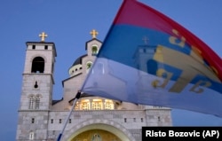 Поддржувач на опозицијата вее старо српско знаме за време на протестот предводен од црквата пред Српската православна црква Христовото Воскресение во Подгорица во август 2020 година.