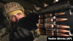 Un soldat ucrainian manevrează o armă automată de mare calibru într-un adăpost militar de pe linia frontului în regiunea Luhansk în estul Ucrainei; 7 februarie 2022. 