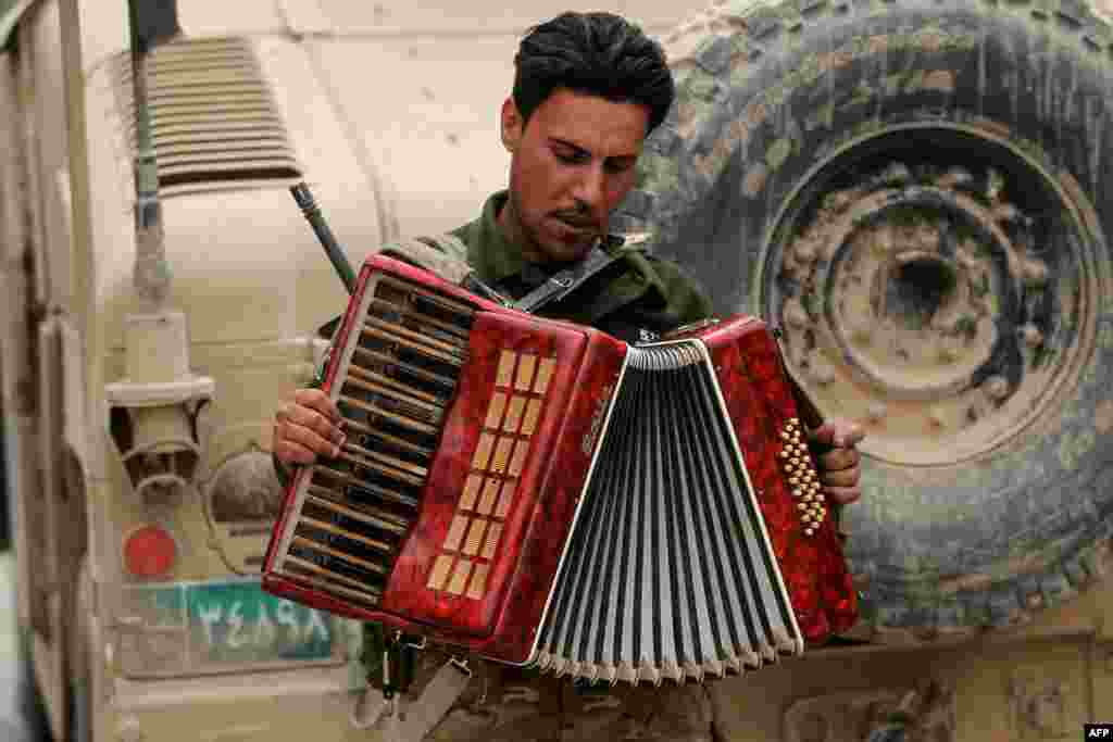 An Iraqi soldier plays with an accordion found on the street while on patrol in the western neighborhood of Tamuz in Mosul. (AFP/Ahmad al-Rubaye)