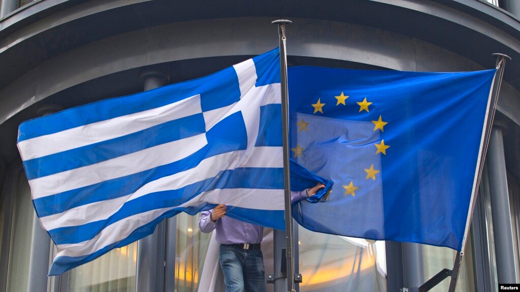 Belgium -- A man adjusts a Greek (L) and a EU flags outside the Greek embassy in Brussels, February 19, 2015