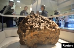 Журналистер өлкетану музейіне қойылған, Шұбаркөлдің түбінен табылған метеорит сынығының жанында тұр. Челябинск, 18 қазан 2013 жыл.
