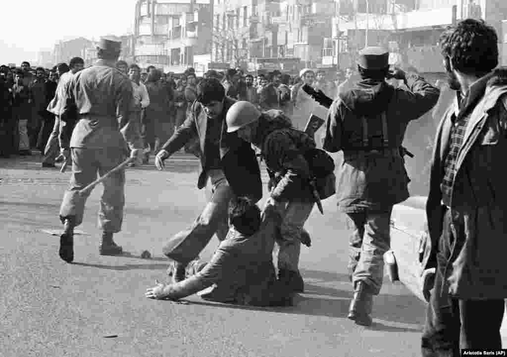 A demonstrator lifted from the ground by a soldier after being clubbed by a stick-wielding army officer (left) during a skirmish in Tehran on January 14, 1979.