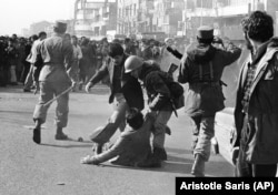 In this Jan. 14, 1979 file picture, a demonstrator is helped up from the ground by a soldier after being clubbed with a stick-weilding army officer, left, during a skirmish between demonstrators and the army in downtown in Tehran.