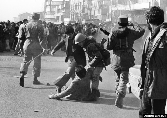 In this Jan. 14, 1979 file picture, a demonstrator is helped up from the ground by a soldier after being clubbed with a stick-weilding army officer, left, during a skirmish between demonstrators and the army in downtown in Tehran.