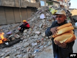 A man carries loaves of bread as a rescue worker takes a break amid buildings damaged in the earthquake in Van.