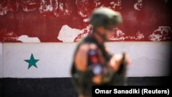 Російський солдат на тлі сирійського прапора в місті Хомс, адміністративному центрі однойменної провінції