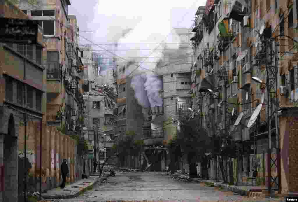 A man stands in an empty street near a burning building hit by a mortar shell fired by Syrian Army soldiers in the Zamalka neighborhood of Damascus. (Reuters/Goran Tomasevic)