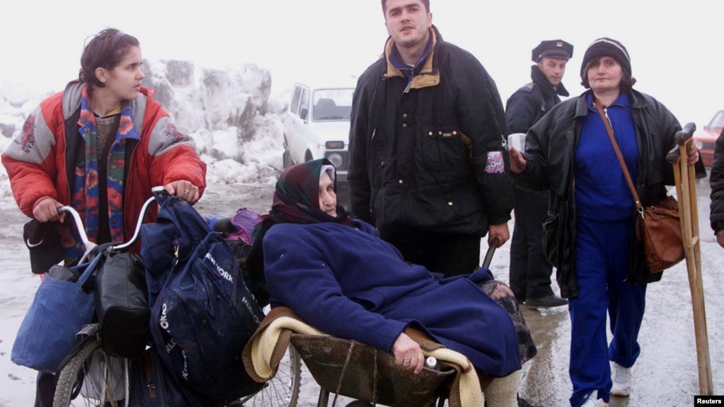 Kosovë: Një grup shqiptarësh pasi arritën në këmbë nga Peja në kufirin me Malin e Zi më 30 mars 1999.Ukrainë: Një grua duke u transportuar me karrocë, në mes të njerëzve që i ikën sulmeve ruse në Irpin, afër Kievit më 9 mars 2022.