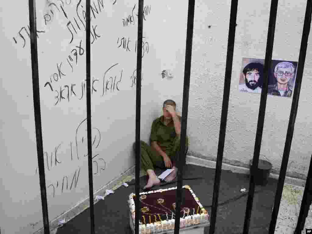 A Palestinian sits in a mock prison cell as he plays the role of missing Israeli soldier Gilad Shalit to mark the fifth anniversary of his capture by Palestinian militants, underneath pictures representing Gilad Schalit (right) and Ron Arad (left), an Israeli airman who disappeared shortly after his plane crashed in Lebanon in 1986.Photo by Hatem Moussa for The AP