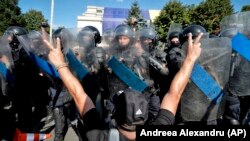 A man flashes victory signs next to a riot police line outside the government headquarters in Bucharest, August 10, 2018.