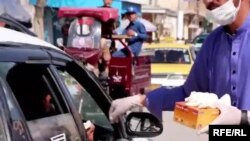آرشیف، یک رضا کار در حال توزیع ماسک و دستکش برای یک راننده در شهر کابل.