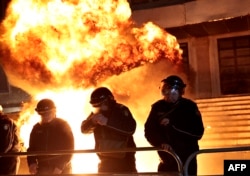 Полицаи пазят входа на сградата, в която се помещава офисът на премиера, докато зад тях избухват коктейли Молотов.