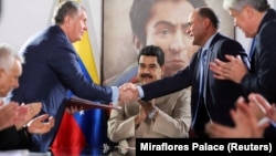 The head of the Russian state oil firm Rosneft, Igor Sechin, (left) shakes hands with the Venezuelan oil minister and the president of the South American country's state oil company PDVSA, Manuel Quevedo, in front of Venezuelan President Nicolas Maduro in Maiquetia in December 2017. 