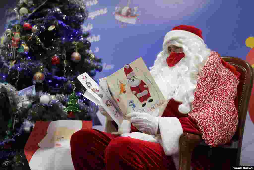 A postal worker dressed as Santa, reads letters to addressed to "Pere Noel" - Father Christmas in French - decorated with love hearts, stickers and glitter, in Libourne, southwest France, Monday, Nov. 23, 2020.