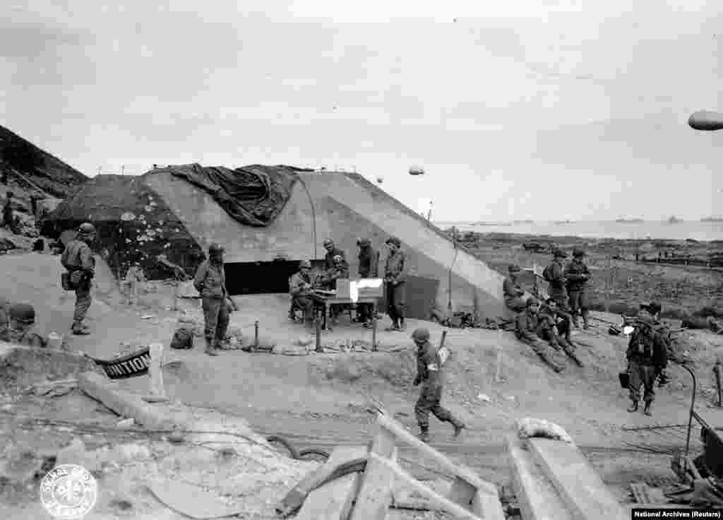 Trupele armatei americane se adună în jurul unui post de semnalizare, folosit de ingineri pe teritoriul unui buncăr german capturat, cu vedere spre Omaha Beach, după aterizările din D-Day lângă Saint Laurent sur Mer, pe 7 iunie 1944