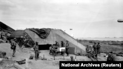 Архіўнае фота. Амэрыканскія вайскоўцы зьбіраюцца каля пункту сувязі на месцы захопленага нямецкага бункера пасьля высадкі каля Сэн-Ляран-сюр-Мэр ў Нармандыі, 7 чэрвеня 1944 году