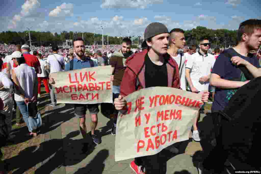 The protester on the right holds a sign that reads: &quot;I&#39;m not a criminal. I have a job.&quot; It is a reference to Lukashenka&#39;s speech on August 12 in which he said, &quot;The core of all these so-called protesters are people with a criminal past, currently unemployed. They have no job, so they can wander in the streets and avenues.&quot;