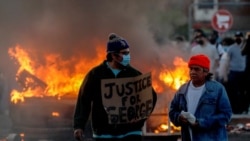 Muškarac koji nosi masku za lice drži natpis 'Pravda za Georga' blizu zapaljenog vozila na parkingu trgovine Target tokom protesta 29 maja 2020.