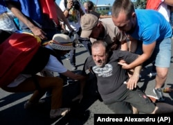 Mai mulți oameni ajută un bărbat rănit în timpul protestelor de la 10 august 2018. La finalul zilei, peste 400 de participanți aveau să fie răniți în confruntările cu forțele de ordine din Capitală.