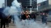 یکی از معترضان در تظاهرات روز شنبه گلوله گاز اشک‌آور را با راکت تنیس دفع می‌کند